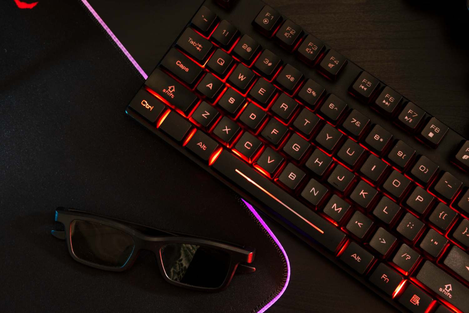 Gracz e-sportowy, Tomasz Nexus Krawczyk, z frustracją patrzy na zalane klawisze swojej klawiatury mechanicznej na tle gamingowego stanowiska, obok widoczny nieszczelny tradycyjny box mod.